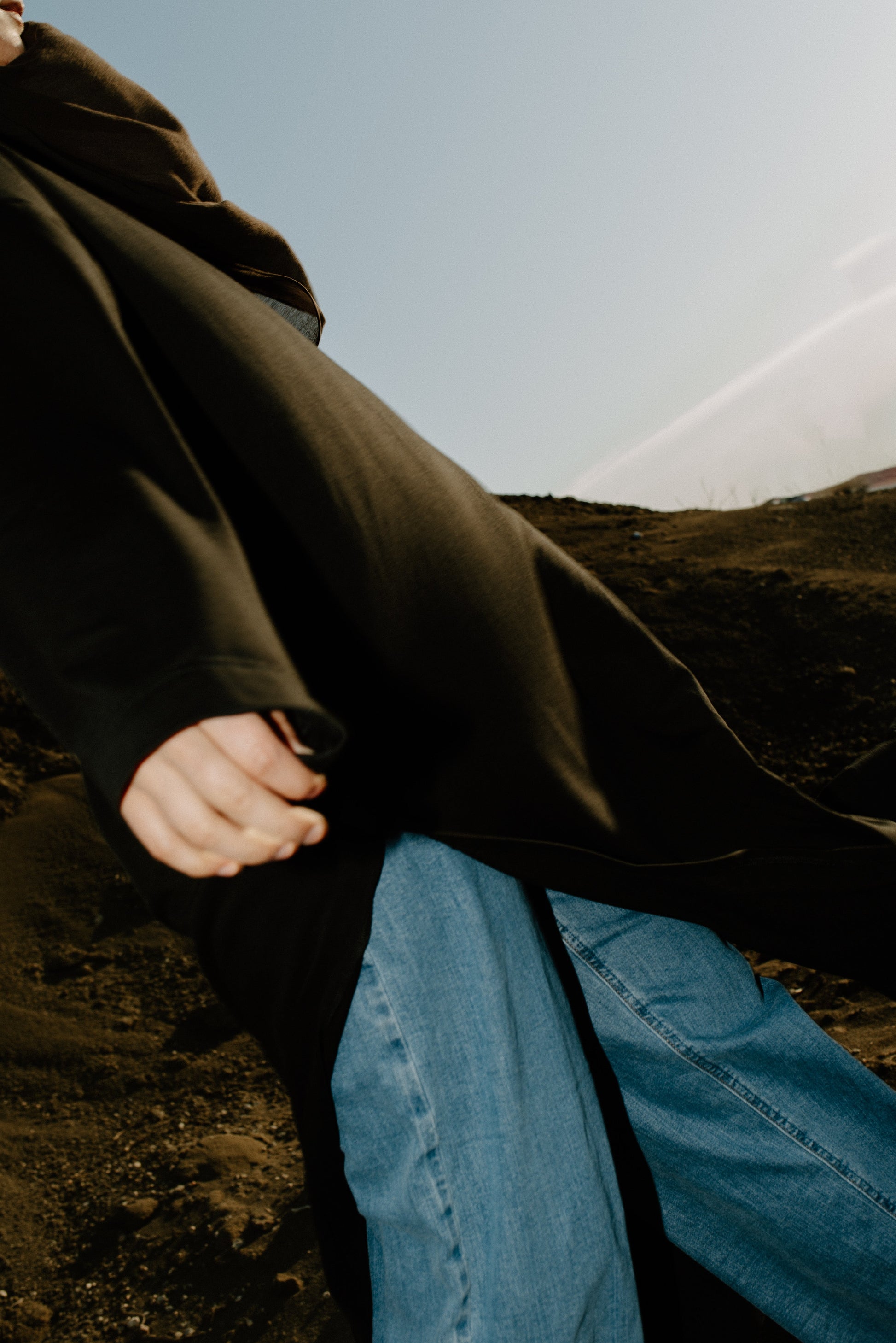Person wearing a black top and blue jeans standing on a rocky landscape with a clear sky.